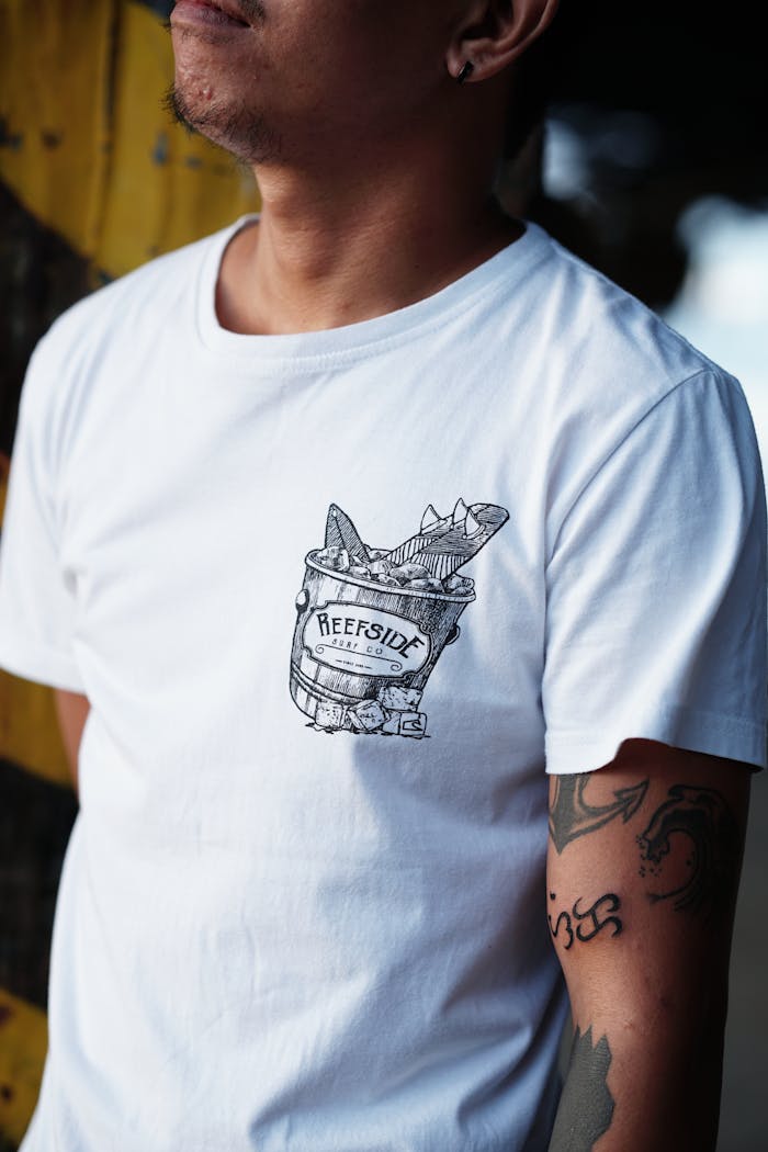 Man wearing a Reefside t-shirt, showcasing tattoos, exuding casual beach style.