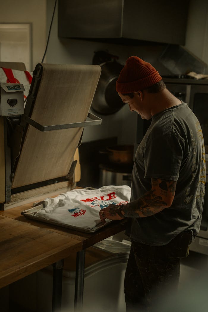 Adult man printing a custom t-shirt using a heat press in a dimly lit workshop.